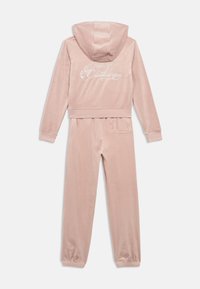 Roza velur trenirka, ki vključuje jakno s kapuco, na kateri je na hrbtni strani napisan "Juicy Couture" v kovinskem napisu, ter elastične manšete na hlačah.