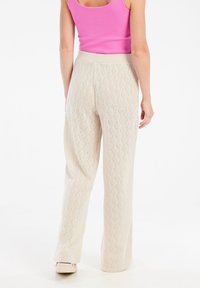 Beige gebreide wijde broek met een diamantpatroon, voorzien van een rekbare tailleband, gecombineerd met een aansluitende roze tanktop.