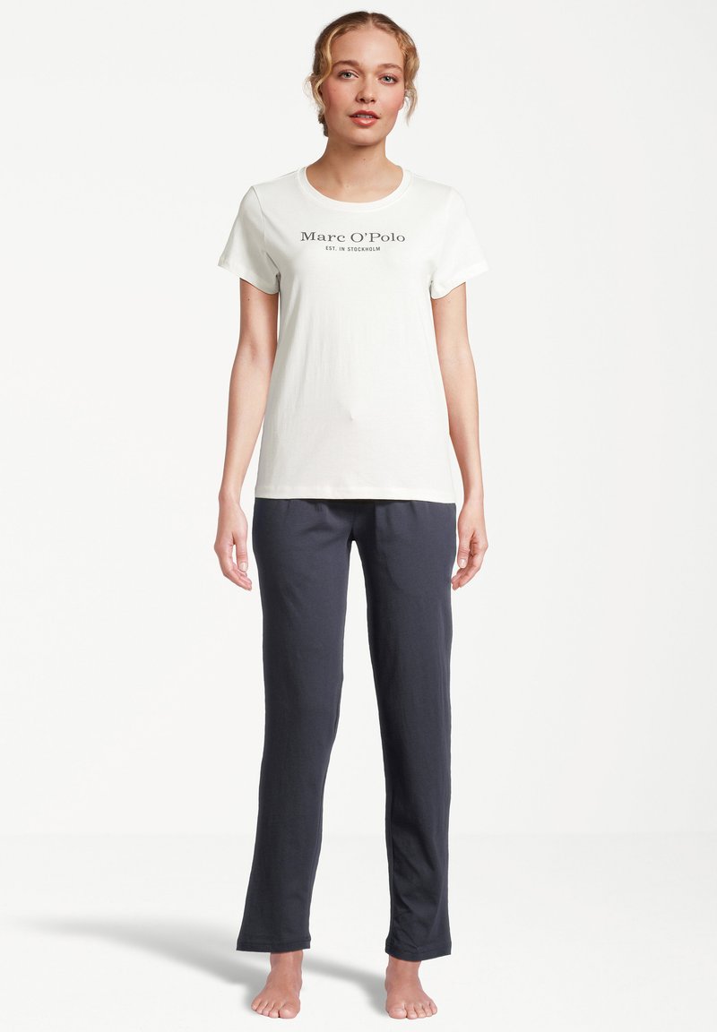 Vit t-shirt med kort ärm med "Marc O'Polo" logotyp, kombinerad med mörkblå, löst sittande byxor; enkel design och tyg.