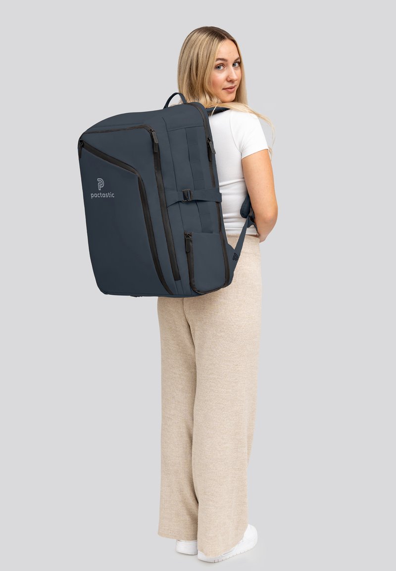 Sac à dos marine avec des accents noirs, grand compartiment principal, poches latérales et bretelles ajustables, porté sur le dos d'une personne.