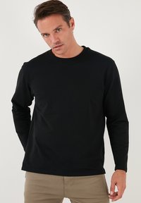 Maglietta nera a maniche lunghe in un materiale morbido con scollatura rotonda, caratterizzata da un design aderente e cuciture minime per un aspetto pulito.