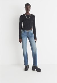 Top de punto negro de manga larga con textura acanalada, combinado con jeans de mezclilla rectos de color azul claro. Zapatos de plataforma negros con tacón grueso.