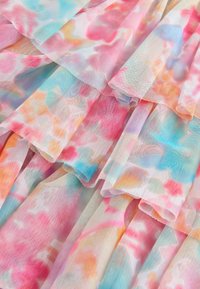 Tissu transparent superposé avec un motif tie-dye aux tons pastel rose, bleu, orange et blanc, montrant des plis doux et une texture.