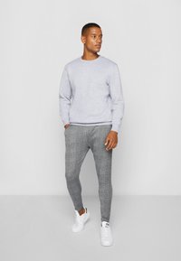 Sweatshirt cinza de gola redonda combinado com calças slim-fit de padrão xadrez, realçado por ténis brancos. Tecido suave, design casual.