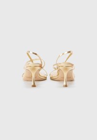Sandali con tacco alto e cinturini dorati, caratterizzati da un tacco affusolato e da sottili cinturini con una superficie liscia e lucida. Design minimalista con una silhouette slanciata.