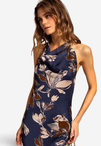 Marineblaues Blumentkleid mit einem Cowl-Ausschnitt, großen Blumenmustern in Beige und Braun sowie einer glatten, fließenden Stoffstruktur.