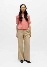 Lichtroze geribd top met korte mouwen, gecombineerd met beige wijde broekspijpen en zwarte schoenen, met een ontspannen pasvorm en gladde texturen.