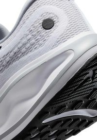 Scarpa sportiva bianca con tomaia in maglia testurizzata, pulsante nero e suola in gomma nera con un design del battistrada a motivo.