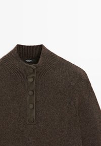 Pull tricoté marron avec un col montant côtelé et une patte de boutonnage comportant quatre boutons ronds. Le matériau semble doux avec une finition texturée.