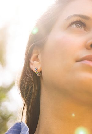 Boucle d'oreille en argent avec des pierres rectangulaires multicolores. Texture lisse avec un design moderne, portée sur l'oreille d'un modèle dans une douce lumière naturelle.
