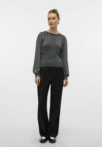 Maglione grigio a coste con maniche lunghe, abbinato a pantaloni ampi neri. L'outfit presenta una texture liscia e una silhouette aderente.