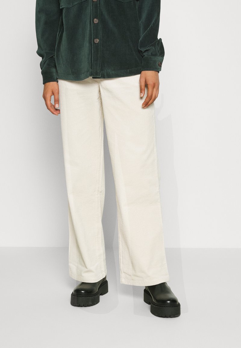 Groene corduroy jas met knopen, gecombineerd met witte wijde corduroy broeken en zwarte chunky platform laarzen. Zachte texturen aanwezig.