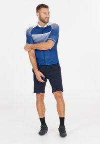 Lyhythelmainen pyöräilypaita tummansinisenä, jossa on valkoisia vaaka-raitaja, yhdistettynä tummiin shortseihin. Materiaali näyttää kevyeltä ja istuvalta.