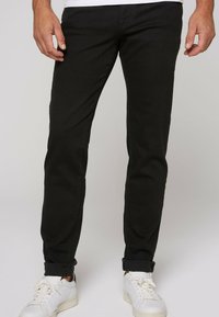 Jeans in denim nero con vestibilità slim e orli arrotolati, abbinati a sneakers bianche. Presentano una texture sottile e un classico design a cinque tasche.