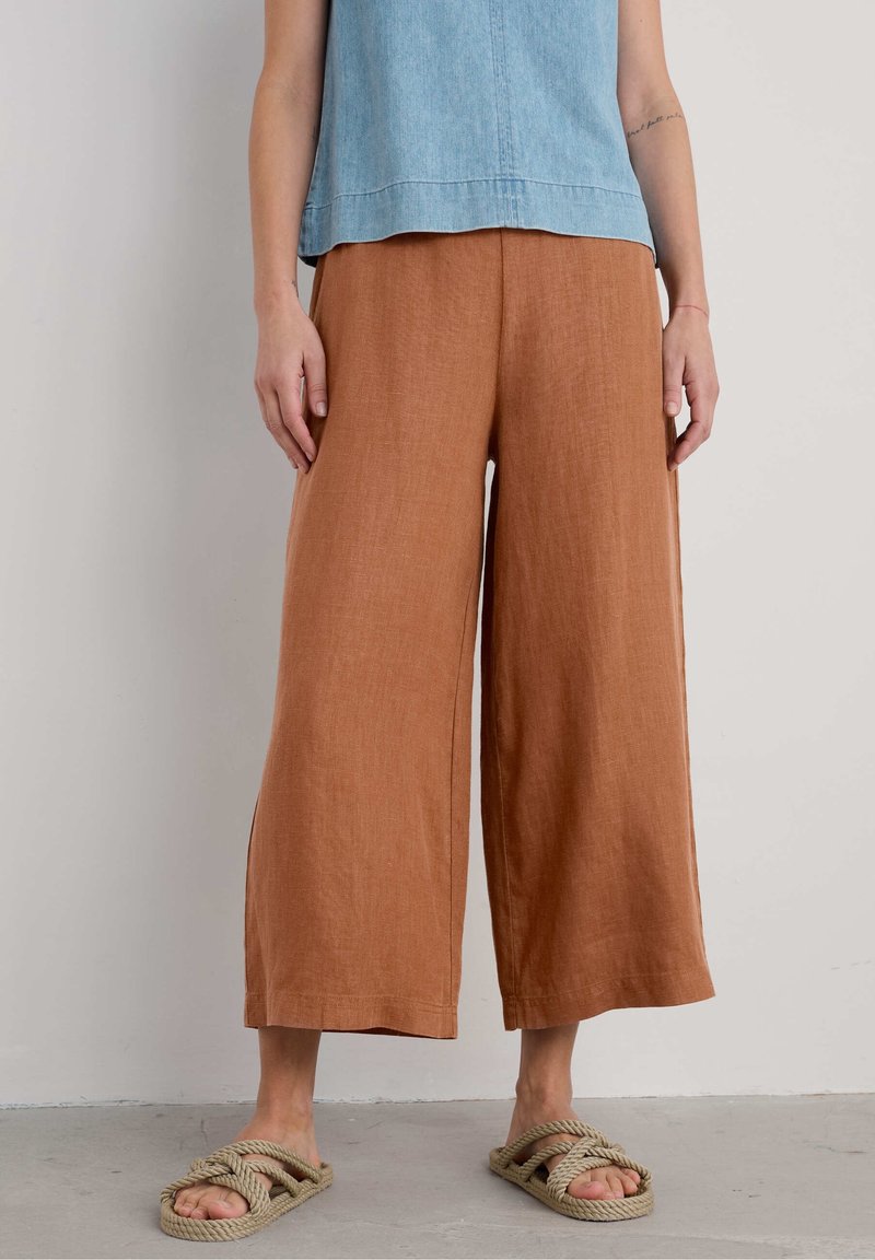 Brown linen wide-leg pants with a textured finish, paired with beige rope sandals. The top is a light blue denim material.
