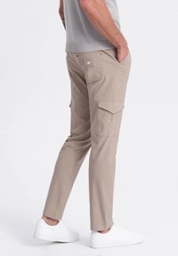 Beżowe spodnie cargo z bocznymi kieszeniami, slim fit, wykonane z mieszanki bawełny, w połączeniu z białymi sneakersami. Prosty i funkcjonalny styl.