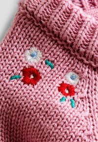 Stickad rosa plagg med ribbad krage, prydd med broderade blommor i rött, vitt och grönt. Texturerat garn ger ett mysigt utseende.