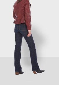 Röd läderjacka, åtsittande design, midjelång. Blå denim bootcut-jeans, mörkt tvättade med bakfickor. Svarta klackade ankelstövlar.