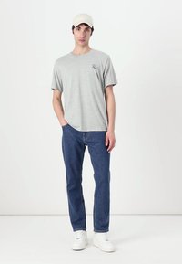 Tricou gri din bumbac cu mâneci scurte, având un mic logo. Asortat cu blugi din denim bleumarin și adidași albi, completat cu o pălărie bej.