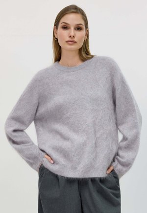 Maglione girocollo grigio chiaro e morbido, realizzato in materiale soffice; presenta maniche lunghe e una vestibilità comoda. Abbinato a pantaloni grigi scuri.