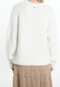 Pull blanc, moelleux et tricoté, avec une coupe ample et des épaules tombantes. Tissu texturé et étiquette de marque discrète à l'arrière du col.