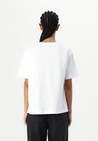 White cotton t-shirt with short sleeves, relaxed fit, crew neckline, and straight hem. Background is neutral and plain.