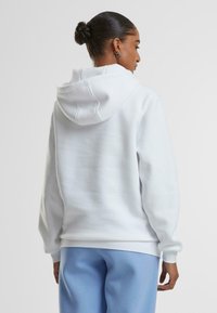 Felpa bianca con cappuccio dal tocco morbido e tasca a marsupio, abbinata a pantaloni della tuta blu chiaro. Il design è casual e dallo stile comodo.