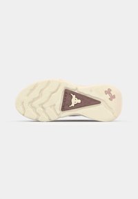 Suela de zapato deportivo en goma blanca y rosa claro con un patrón de tracción texturizado. Detalle del logo en marrón oscuro en el talón y en el inserto triangular.