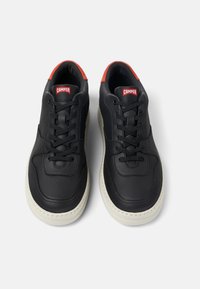 Svarta lädersneakers med röda accenter och vita gummisulor. Har en rund tå och framknäppning, med rena linjer och stickningar.