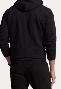 Svart huvtröja med långa ärmar och ribbade muddar. Slät textur utan synliga logotyper eller mönster, sedd bakifrån.