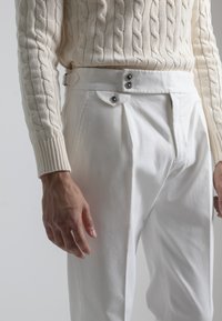 Pantalones de algodón blancos con una cintura alta, que cuentan con dos botones negros y un acento de solapa en la parte delantera. Suéter de punto trenzado en crema con textura.