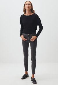 Chemise noire à manches longues, jean gris slim-fit et mocassins noirs. Texture lisse, design décontracté, avec un col rond et des détails subtils.