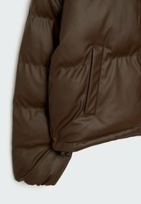 Giacca a vento marrone con una finitura liscia e lucida. Presenta una tasca laterale e polsini a coste, sottolineando la texture trapuntata e il design isolato.