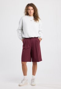 Sweatshirt gris avec texte brodé, associé à un short plissé bordeaux. Des baskets blanches et des chaussettes côtelées complètent le look.