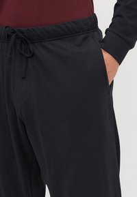Schwarze Jogginghosen mit elastischem Bund und Kordelzug. Verfügt über seitliche Taschen und eine weiche, glatte Textur.