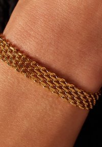 Gouden kettingarmband met in elkaar grijpende ovale schakels, een soepele textuur en een gelaagd ontwerp dat om een pols gewikkeld is.