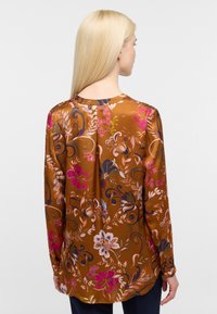 Brun langærmet bluse med et farverigt blomsterprint i pink, blå og grønne nuancer, glat tekstur og rund halsudskæring.