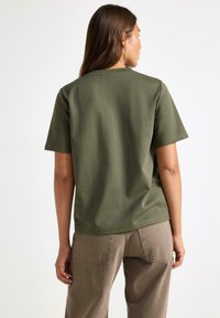 Olive green t-shirt bawełniany o luźnym kroju, z krótkimi rękawami i okrągłym dekoltem. Tekstura jest gładka i nieco elastyczna.
