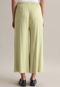 Hellgrüne, weite Hosen aus weichem, leichtem Stoff mit einem elastischen Bund und einer glatten Textur, die an den Knöcheln endet.