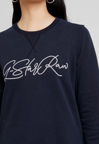 Felpa blu navy realizzata in morbido cotone, con un logo bianco ricamato in corsivo sul petto e un classico collo a giro.