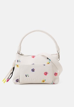Sac à main blanc avec anse tressée, petits imprimés floraux colorés, poche zippée à l'avant et pompons décoratifs aux extrémités jaunes et roses.