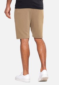 Knie kurze, gerippte beige Shorts mit einem elastischen Bund, kombiniert mit weißen Turnschuhen. Sichtbare Beinmuskeln und weicher Stofftextur.