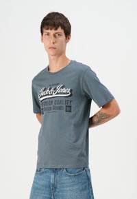 Grå bomull T-skjorte med fronttrykk av teksten "Jack & Jones" og "Superior Quality Denim Goods" i kontrastfarger. Korte ermer.