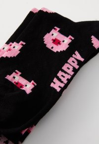 Svarta strumpor med ljusrosa griskonst och ordet "HAPPY" i rosa, tillverkade av ett mjukt stickat material med en slät textur.