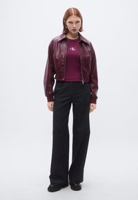 Bomberjacke aus burgunderrotem Leder mit Reißverschluss, kombiniert mit einem figurbetonten weinroten T-Shirt und dunklen, weit geschnittenen Jeans, getragen mit schwarzen Plateau-Schuhen.