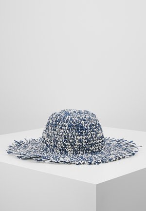 Breedgerande gevlochten strohoed met blauw-witte verstrengelde vezels en rafelige randen, tentoongesteld op een wit voetstuk.