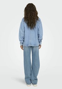 Chaqueta de mezclilla azul claro con corte oversize, que presenta mangas largas y dobladillo recto, combinada con pantalones de mezclilla de pierna ancha.