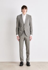 Abito a quadri grigio chiaro con blazer su misura e pantaloni coordinati. Accompagnato da una camicia bianca e scarpe nere massicce. Texture liscia.