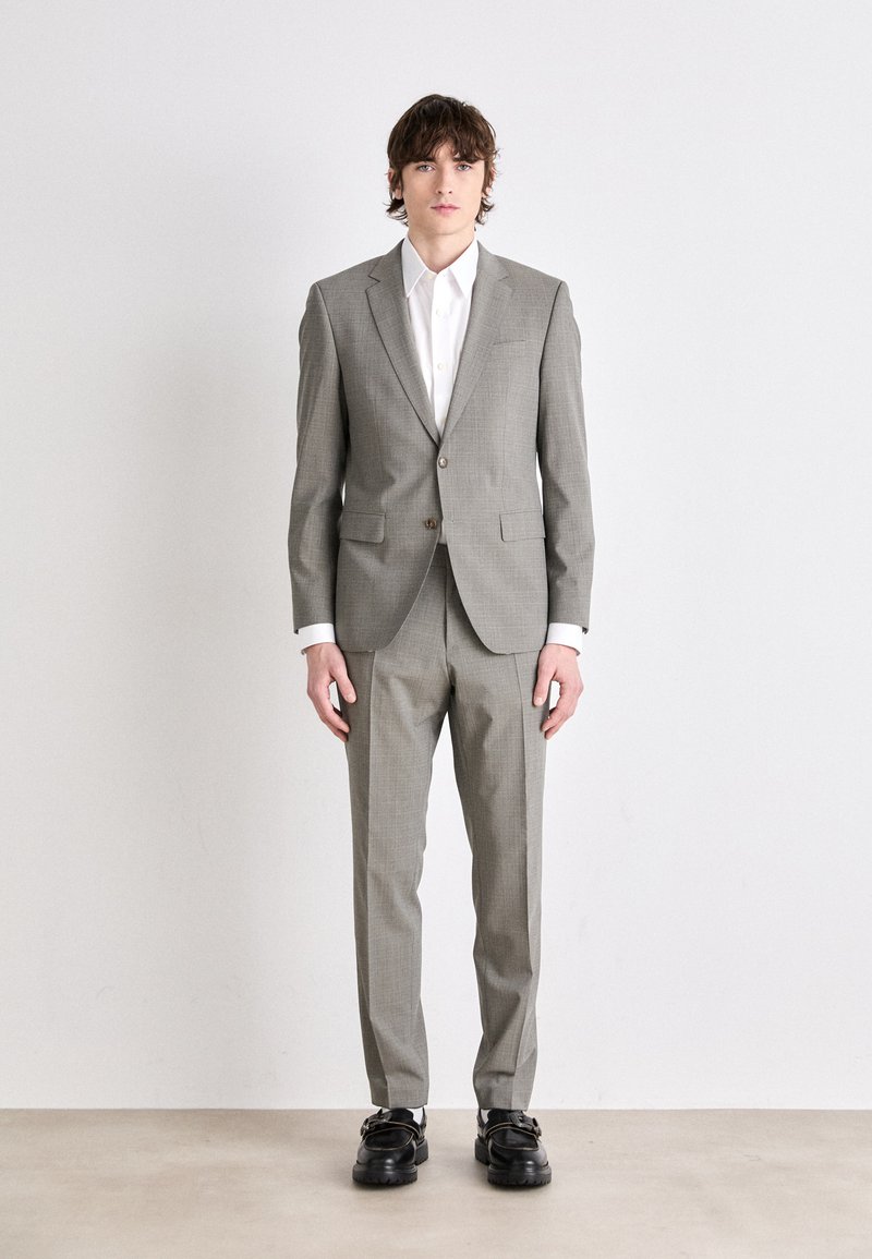 Abito a quadri grigio chiaro con blazer su misura e pantaloni coordinati. Accompagnato da una camicia bianca e scarpe nere massicce. Texture liscia.