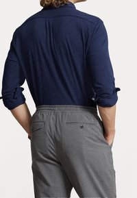 Marinblå skjorta med knappar och uppvikta ärmar, i kombination med grå byxor med elastisk midja och bakfickor med knäppning.